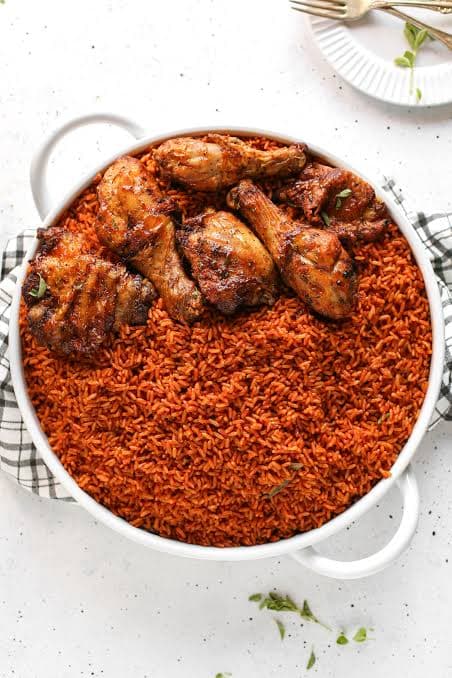 Smoky party jollof rice with grilled chicken and fried plantain on an enamel plate
